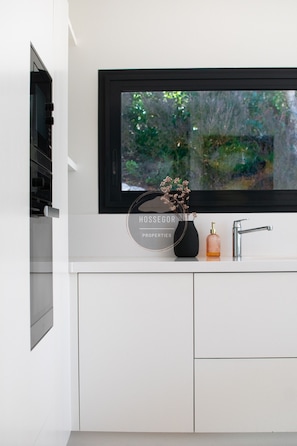 A modern kitchen with a built-in oven, a window with a view of greenery, and a sink with a faucet. - Villa Balis - Seignosse - Pool - Golf - Beach (Seignosse)