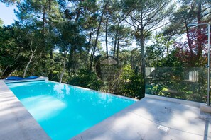 Ein Swimmingpool mit glasklarer, blauer Wasseroberfläche, umgeben von Bäumen und einer Glasumrandung.