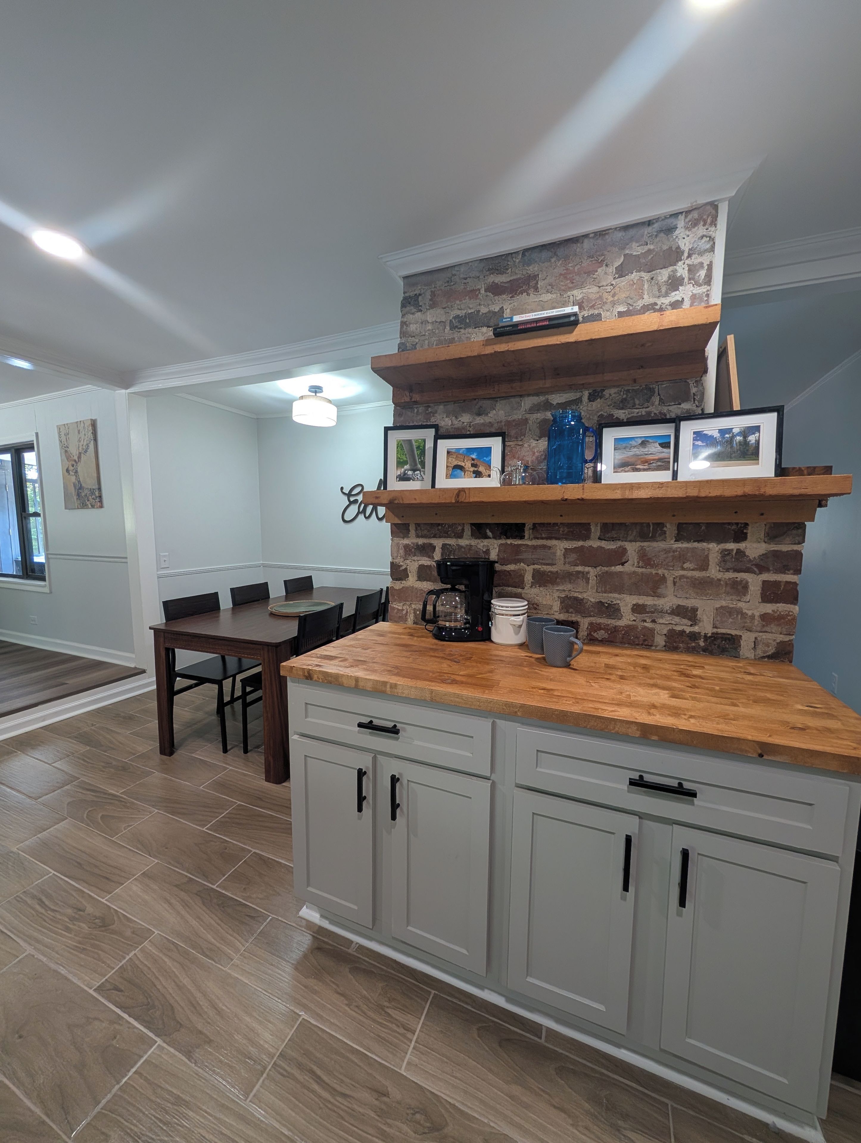A kitchen with a brick wall, wooden shelves, and a dining area with a table and chairs.