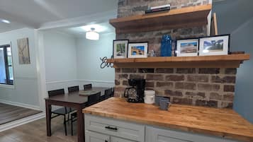 A kitchen with a brick wall, wooden shelves, and a dining area with a table and chairs.