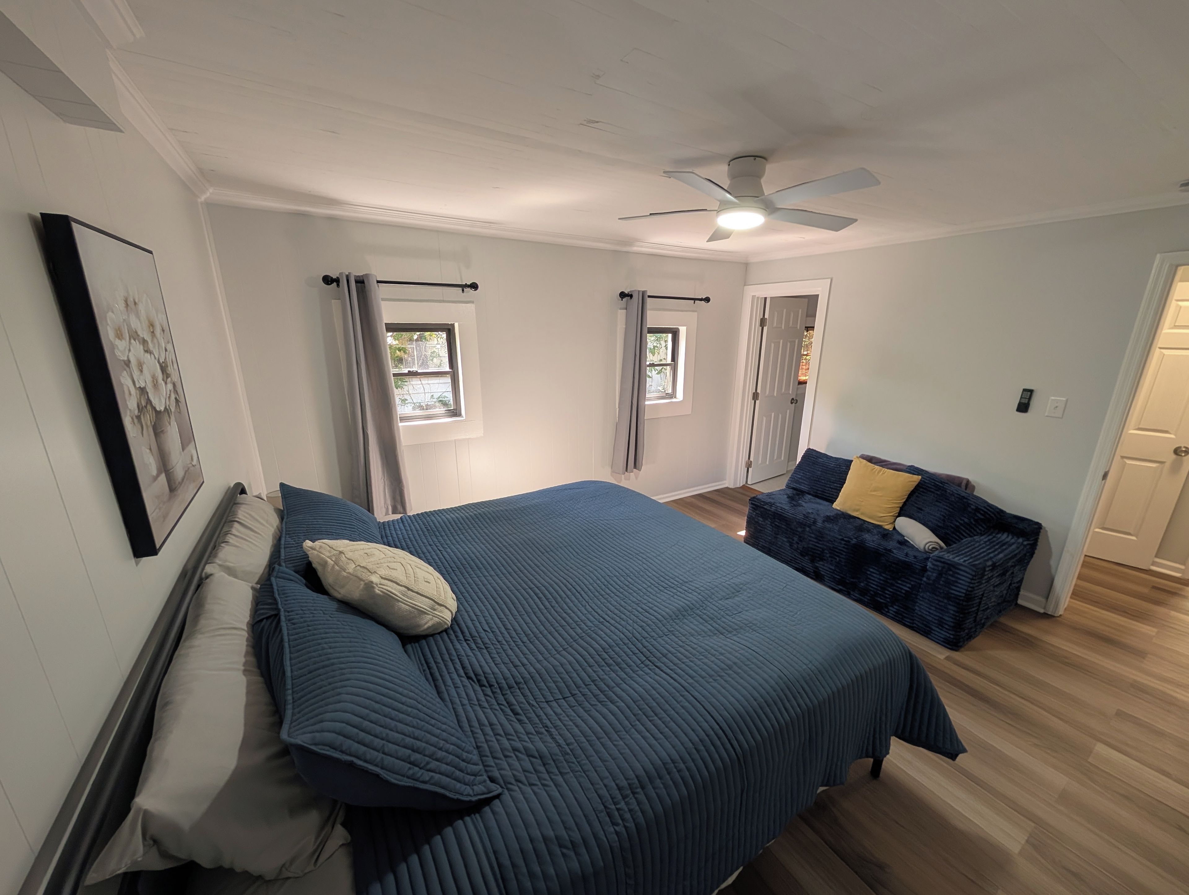 A bedroom with a bed, a blue sofa, a ceiling fan, and a window.