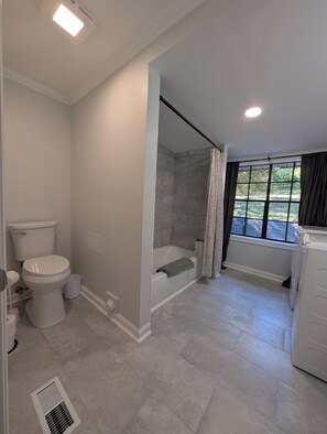 Baño con inodoro, ducha, bañera y ventana con cortinas.
