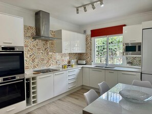 A modern kitchen with white cabinets, a stainless steel range hood, a built-in oven, a microwave, and a window with a view of greenery. - Villa 'Miramar Burriana Nerja' with Sea View, Wi-Fi and Air Conditioning (Nerja)