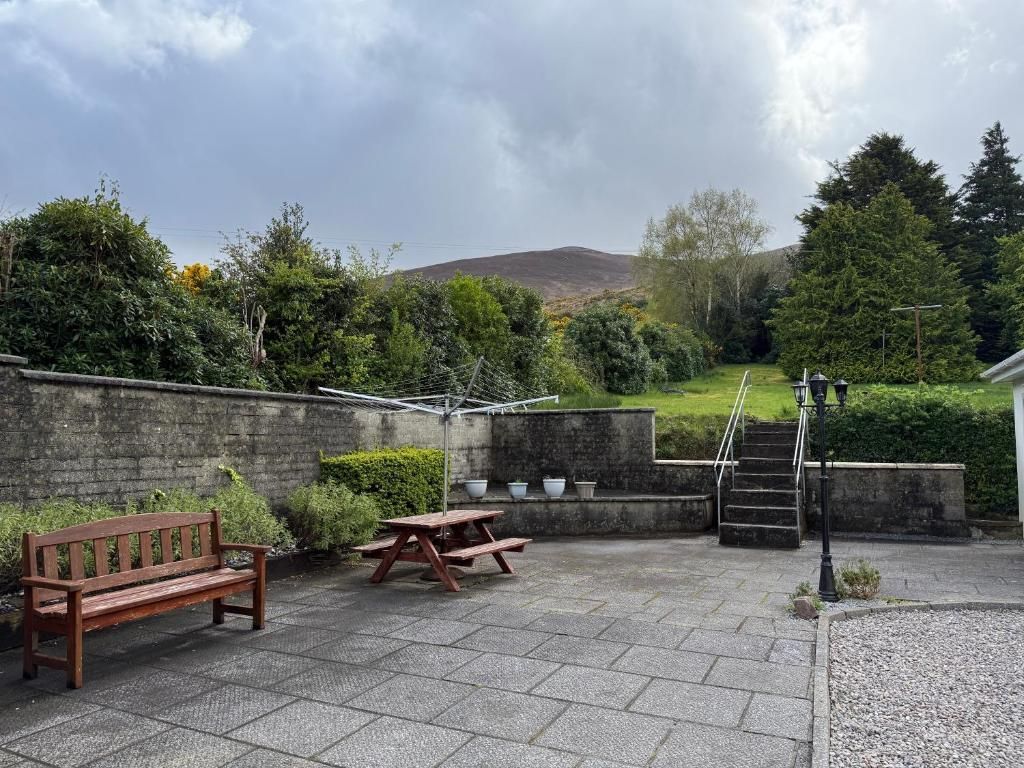 An outdoor patio area with a wooden bench, picnic table, and steps leading to a grassy hill.