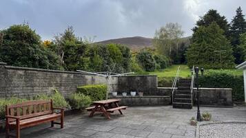An outdoor patio area with a wooden bench, picnic table, and steps leading to a grassy hill.