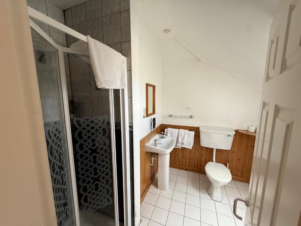 A bathroom with a shower, toilet, sink, and wooden paneling.