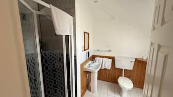 A bathroom with a shower, toilet, sink, and wooden paneling.