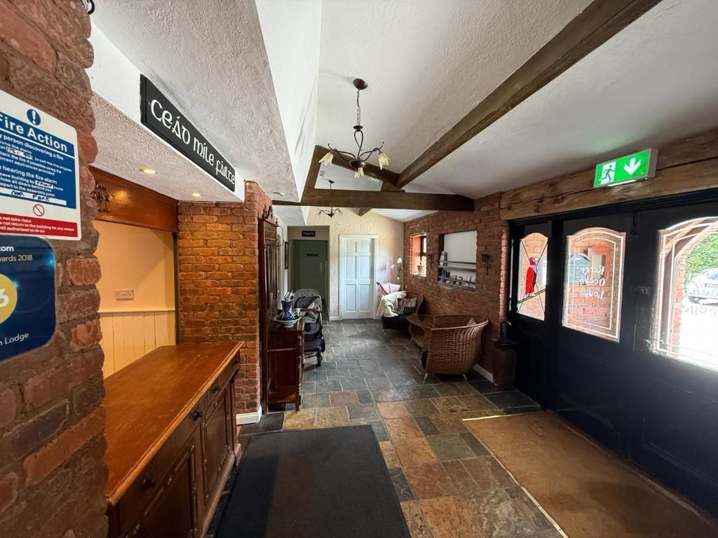 A hotel lobby with a brick wall, a reception desk, a staircase, and a door with a green exit sign.