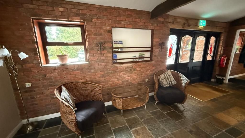 A room with brick walls, a window with a plant, wicker chairs, a small table, and a door with glass panels.