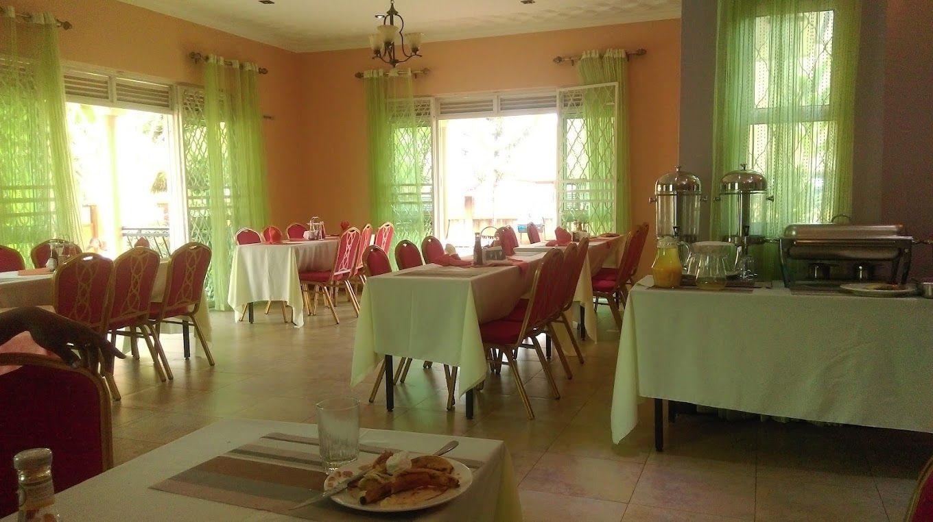 Un comedor con varias mesas y sillas, una mesa de buffet y ventanas grandes con cortinas.