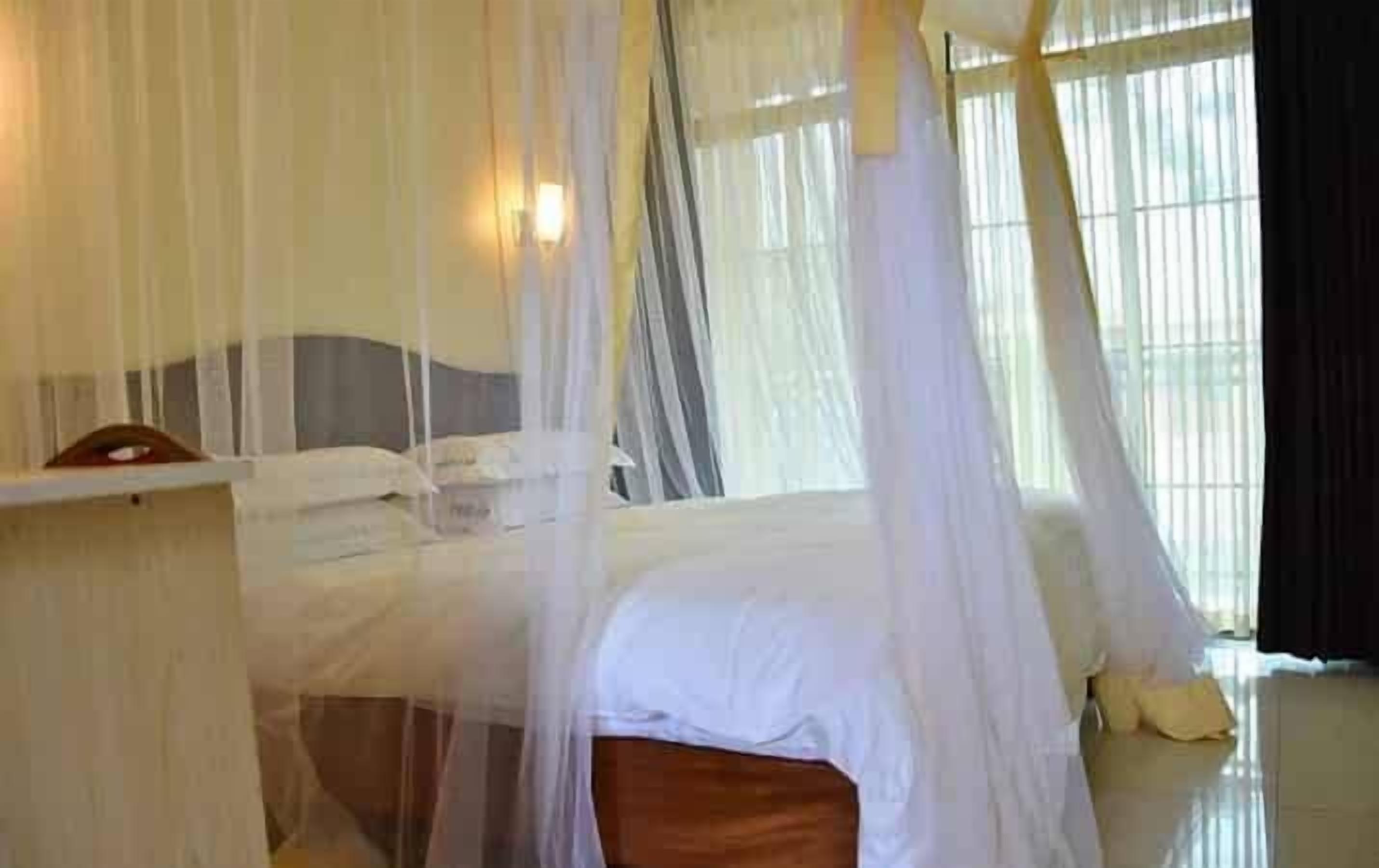 A bed with a canopy, a bedside table, and a window with curtains.