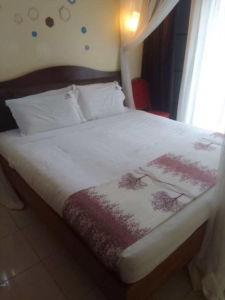 Una cama con una colcha blanca y un plaid decorativo, un cabecero de madera y una pared con arte mural geométrico.