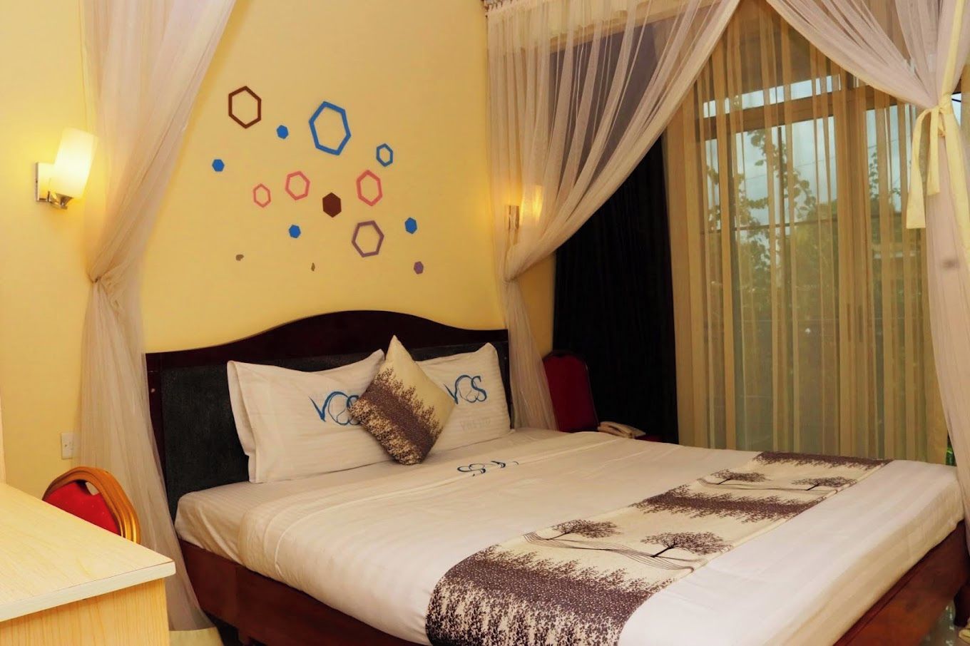 Una habitación de hotel con una cama, una mesita de noche, una lámpara y un ventanal con cortinas.