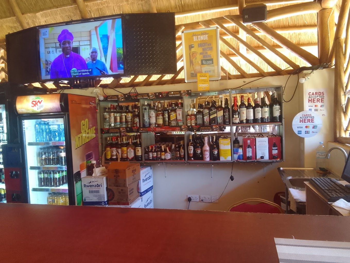 A bar area with a television screen, shelves of liquor, and a sign indicating card acceptance.