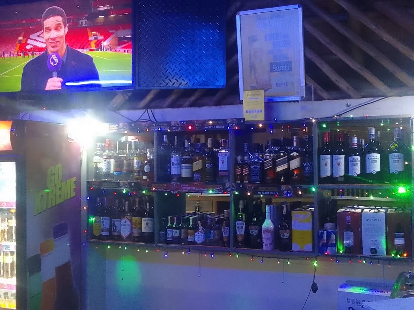 A bar area with shelves of liquor bottles and a television screen displaying a sports event.