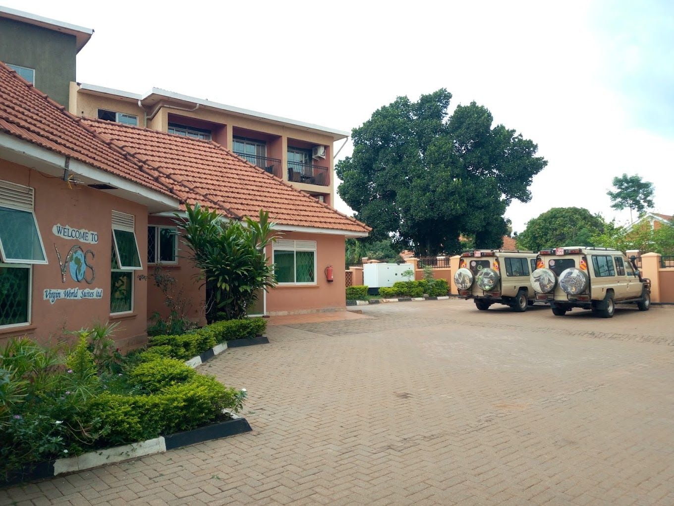 A building with a sign reading 'Welcome to Virgin World Suites Ltd.' There are two vehicles parked in front.