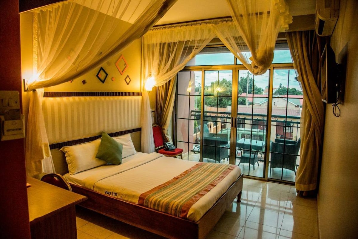 Een hotelkamer met een bed, een bureau, een stoel, een televisie en een balkon met uitzicht.