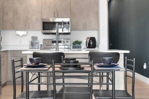A modern kitchen with stainless steel appliances, a dining area with black chairs and a table, and a black door. - Serene loft style 2Bth | Gym | Parking | Workspace (Dallas)
