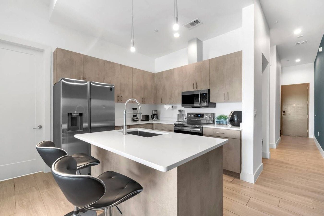 A modern kitchen with a central island, stainless steel appliances, and bar stools.