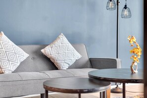 A modern living room with a grey sofa, patterned cushions, a round coffee table, and a vase with flowers. - Serene loft style 2Bth | Gym | Parking | Workspace (Dallas)