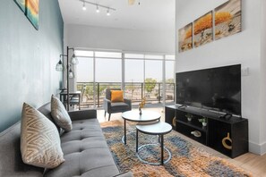 A modern living room with a sofa, coffee table, and TV, large windows, and a balcony. - Serene loft style 2Bth | Gym | Parking | Workspace (Dallas)