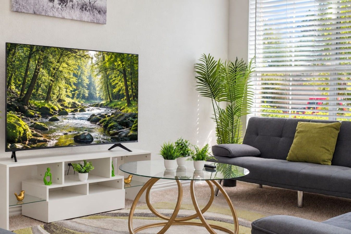 A modern living room with a flat-screen TV, a grey sofa, a glass coffee table, and a white entertainment unit.