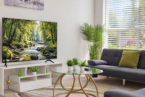 Ein modernes Wohnzimmer mit einem Flachbildfernseher, einem grauen Sofa, einem Glastisch und einer weißen Unterhaltungsanlage.