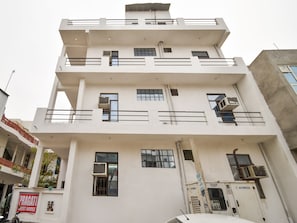 Un edificio de varios pisos con balcones, unidades de aire acondicionado y señalización de una casa de huéspedes.
