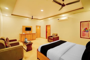 Ein Hotelzimmer mit Bett, Schreibtisch, Sessel, Fernseher und Deckenventilator.