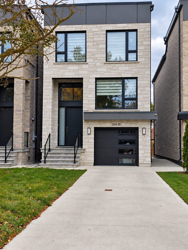 A modern two-story residential building with a garage, a front entrance with steps, and a clear driveway.