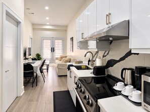 A modern kitchen with white cabinets, a stove, a sink, and a dining area with a table and chairs.