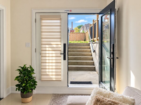 A residential entryway with a sliding glass door, a staircase leading outside, a potted plant, and a white cushioned bench.