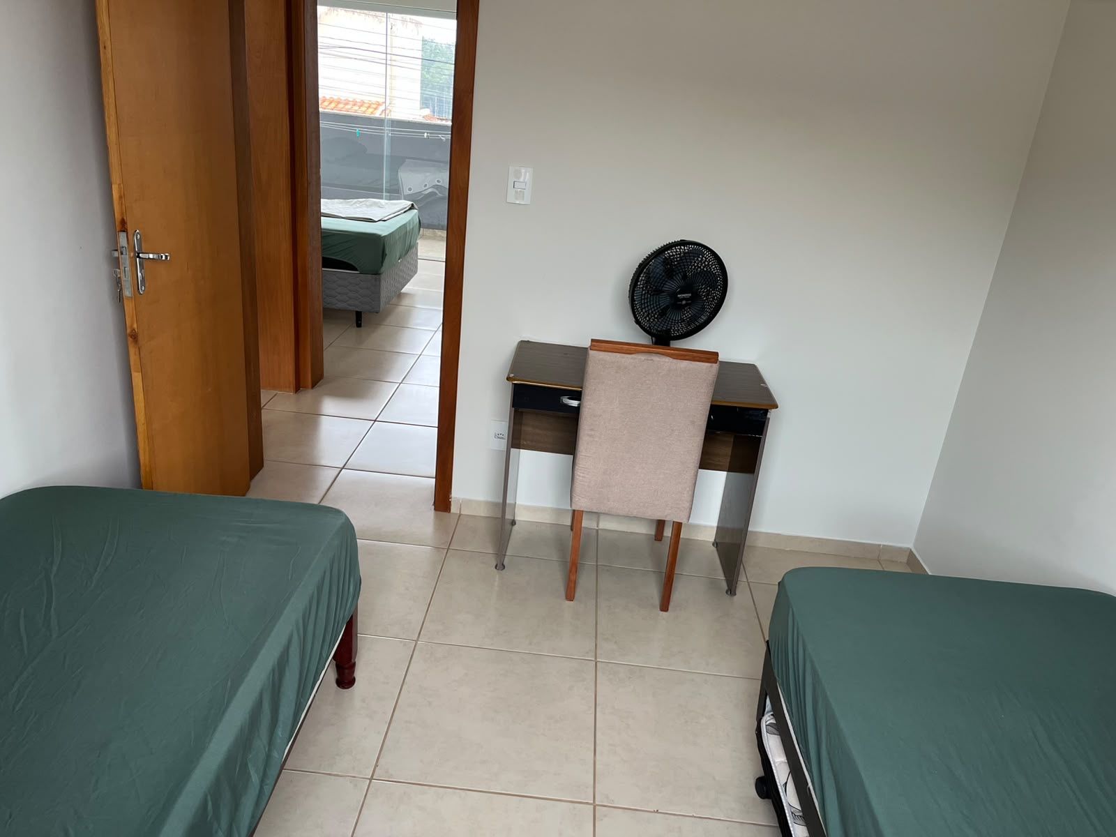 A room with two beds, a desk with a chair, and a fan.