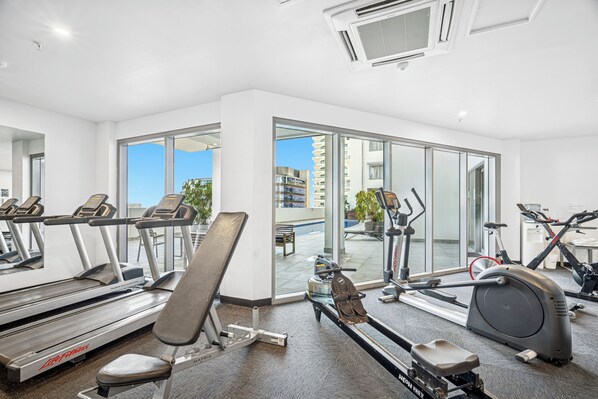 A modern gym with treadmills, a bench press, and a rowing machine. - Harbour Glimpses Central CBD Stay with Pool and Gym (Darwin)