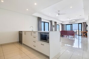 A modern kitchen with a built-in microwave, a dishwasher, and a dining area with a table and chairs. - Harbour Glimpses Central CBD Stay with Pool and Gym (Darwin)