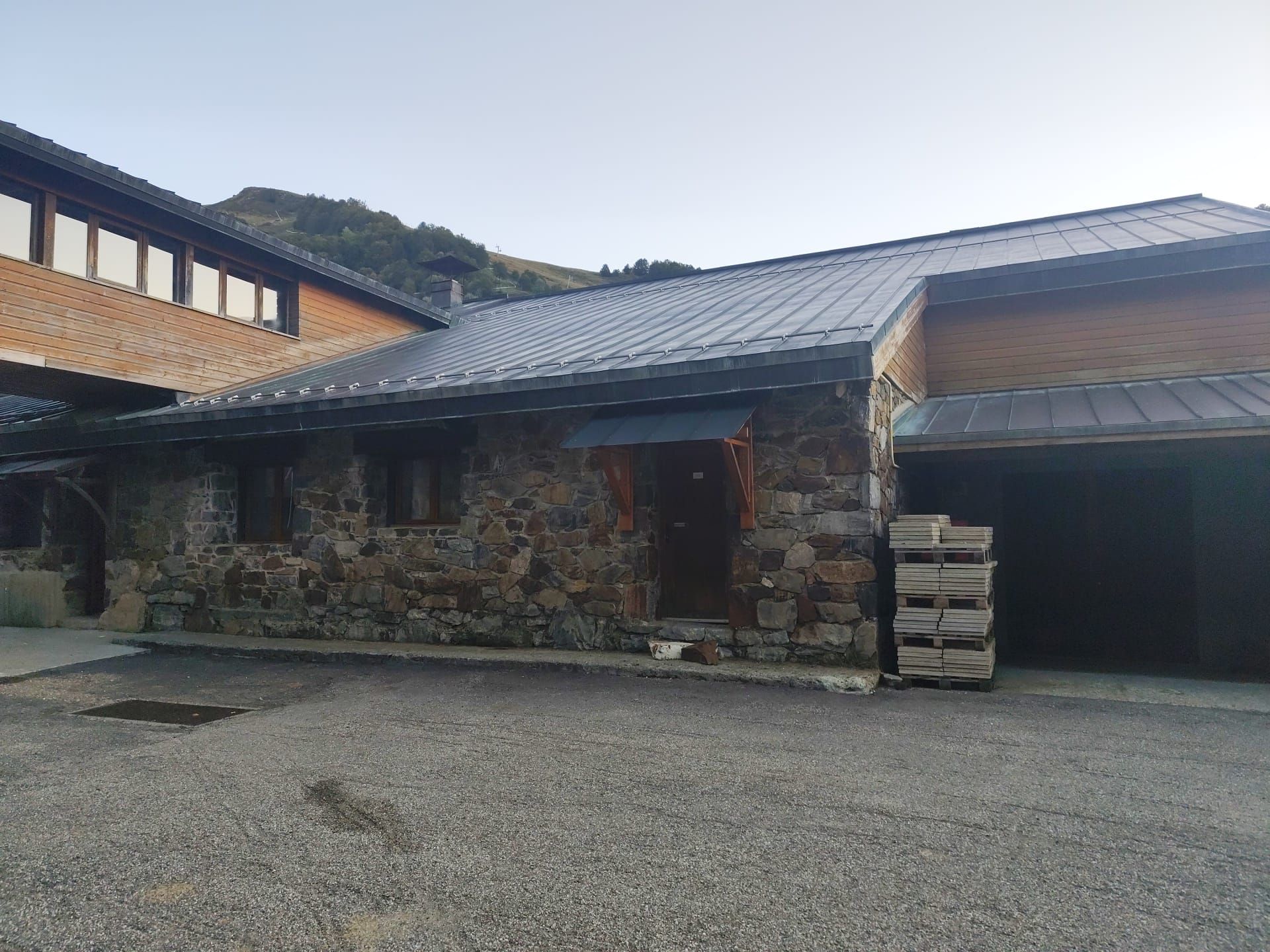 Ein Gebäude aus Stein mit einem Metall-Dach, einer Holzterrasse und einer Schotterauffahrt.