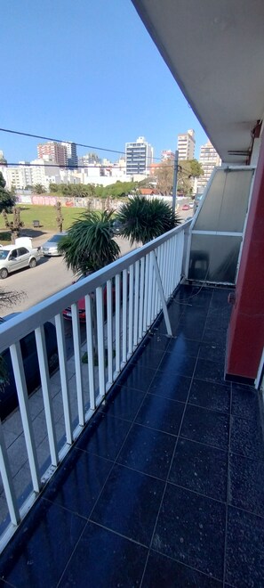 En balkon med gelænder i hvidt, udsigt over bybilledet og en flisegulv.