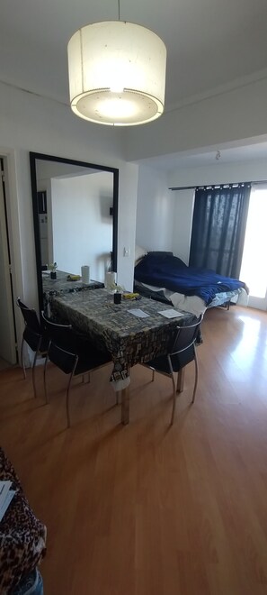 Ein Essbereich mit Tisch und Stühlen, einer Deckenleuchte und Blick auf ein Schlafzimmer mit Bett und Vorhängen.