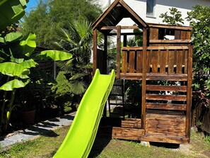 Een houten speelhuisje met een glijbaan in een tuin.
