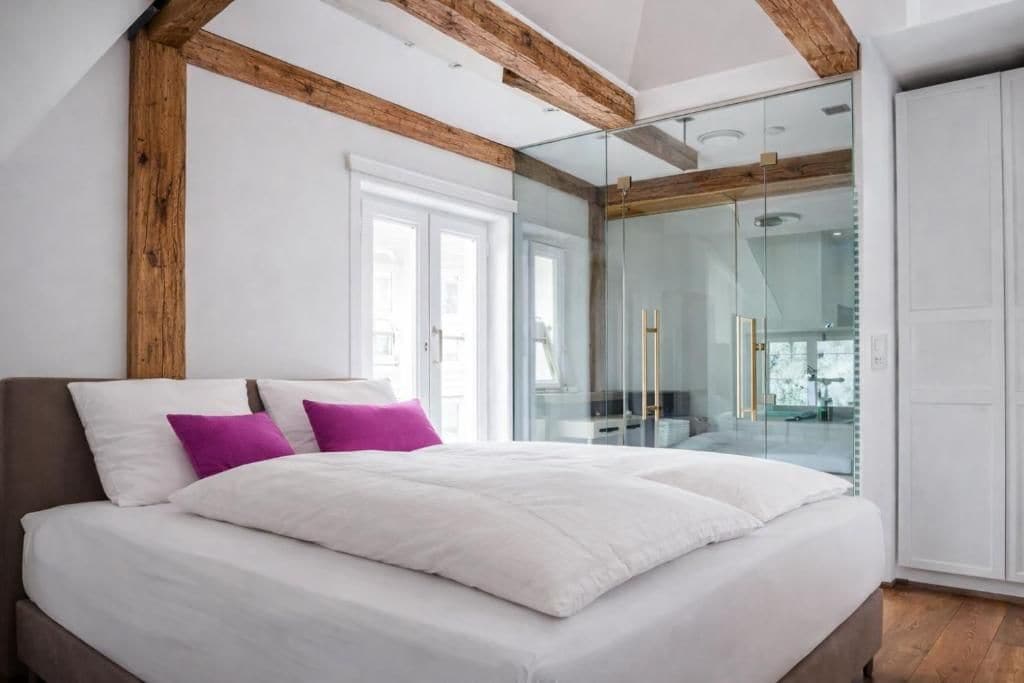 Une chambre dotée d’un grand lit, d’une douche à parois de verre et de poutres apparentes.