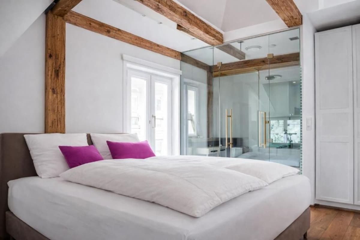Una camera da letto con un letto grande, un box doccia in vetro e travi a vista in legno.