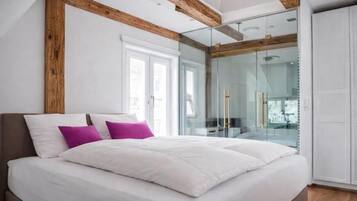 Une chambre dotée d’un grand lit, d’une douche à parois de verre et de poutres apparentes.