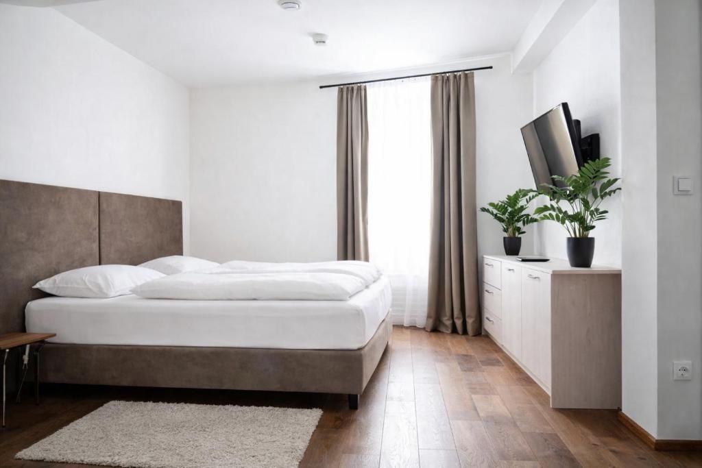 Quarto moderno com cama, mesa de cabeceira, televisão e planta em vaso.