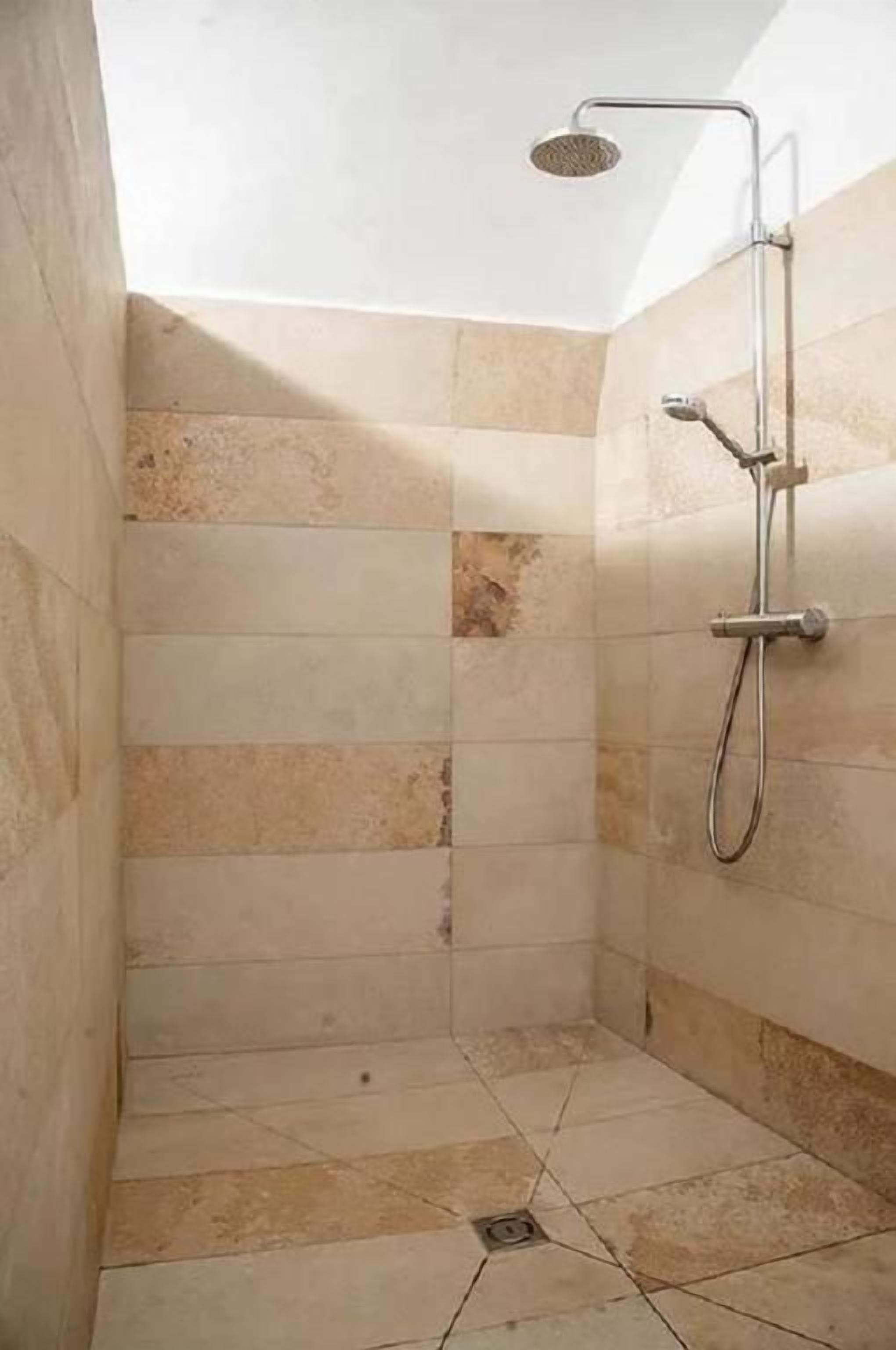 A shower area with tiled walls and floor, a handheld showerhead, and a wall-mounted faucet.