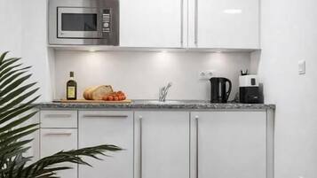 A compact kitchen with white cabinets, a microwave, a coffee maker, and a bread loaf on the counter.