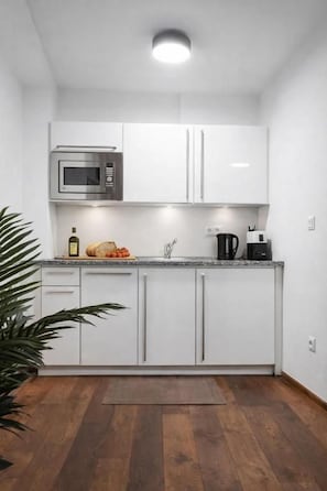Una cucina compatta con mobili bianchi, un forno a microonde, una macchina da caffè e una pagnotta sul piano di lavoro.