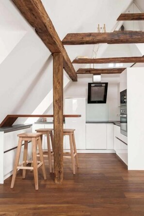A kitchen with white cabinets, wooden stools, and exposed wooden beams. - Urban Luxury Apartments (Graz)