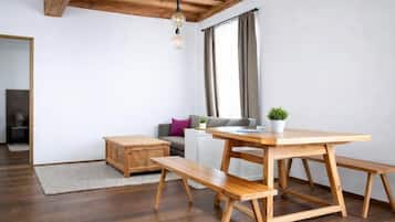 Espaço de estar moderno com mesa de jantar de madeira, bancos, sofá e pequena mesa lateral com uma planta.