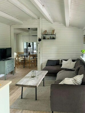 A living room with a sofa, a coffee table, a television, and a dining area with chairs and a table. - Summer cottage with conservatory and enclosed plot (Nykøbing Sjælland)