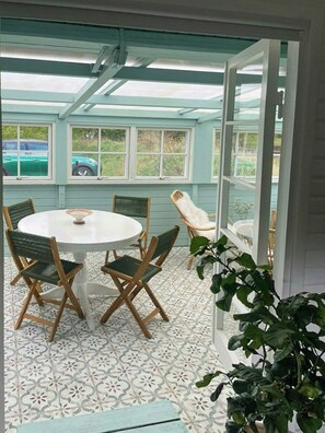A covered patio area with a round table and chairs, a white chair, and a potted plant. - Summer cottage with conservatory and enclosed plot (Nykøbing Sjælland)